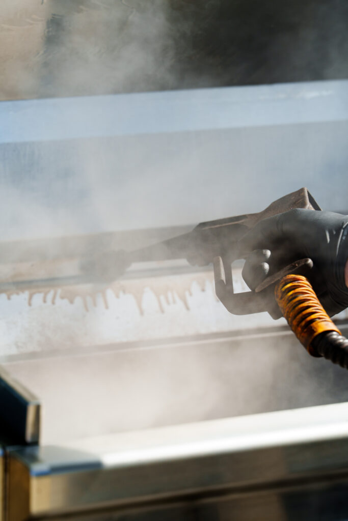 A Firemetal worker removing grease buildup from a grill during a routine grill cleaning session